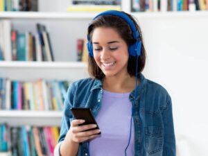 a girl with blue headphones smiling at her phone while listening to a podcast